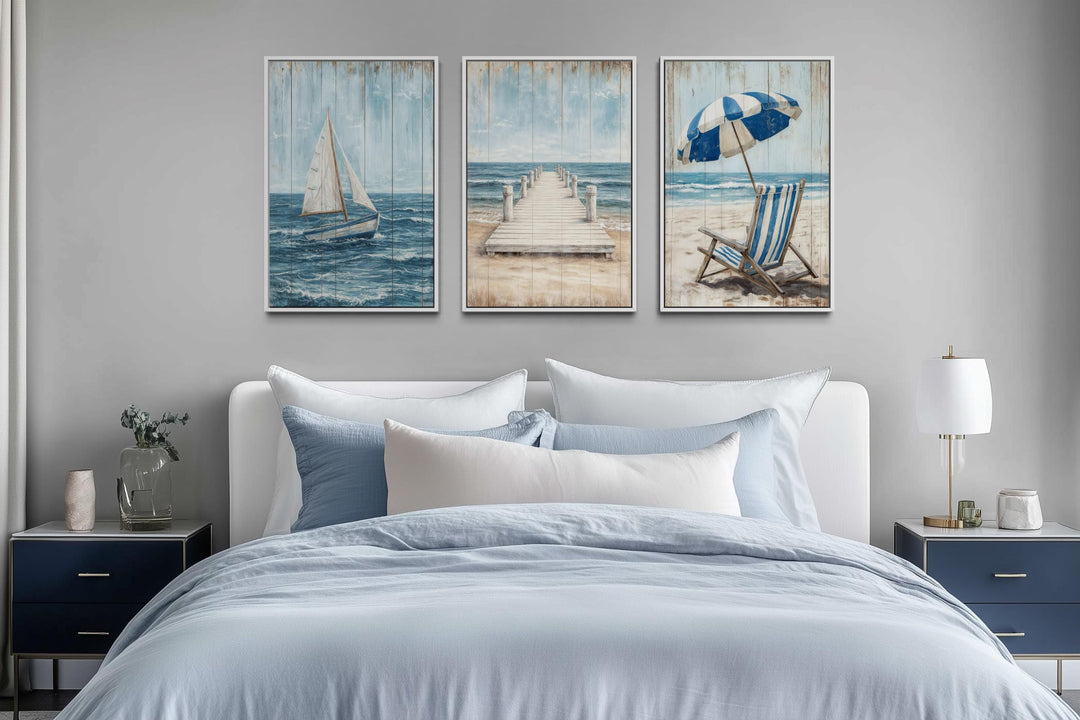 Three-piece coastal wall art set featuring a sailboat, pier, and beach chair above a bed.