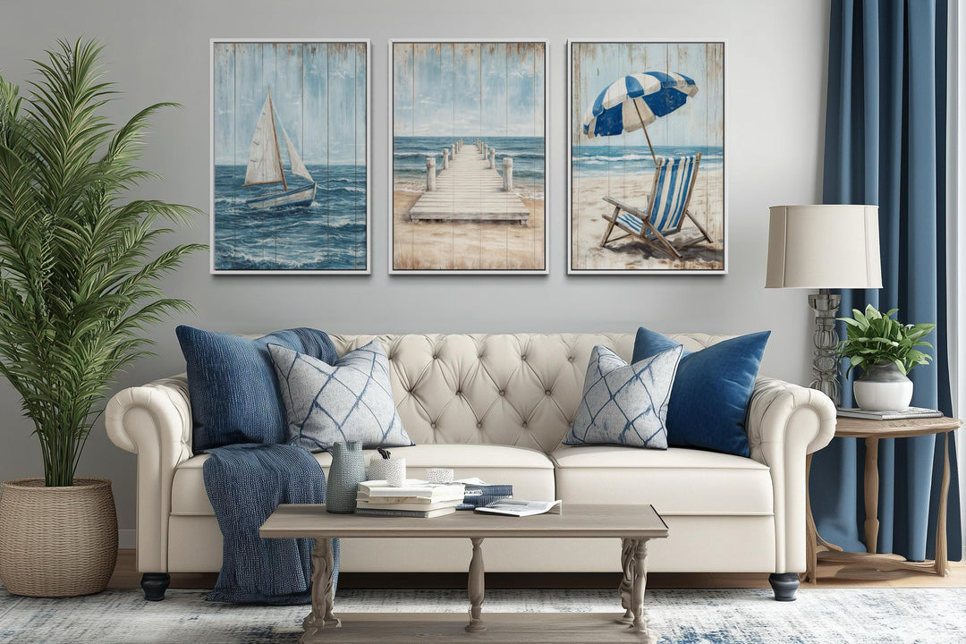 Three-piece coastal wall art set featuring a sailboat, pier, and beach chair above a cream sofa.