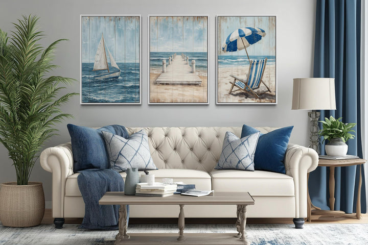 Three-piece coastal wall art set featuring a sailboat, pier, and beach chair above a cream sofa.