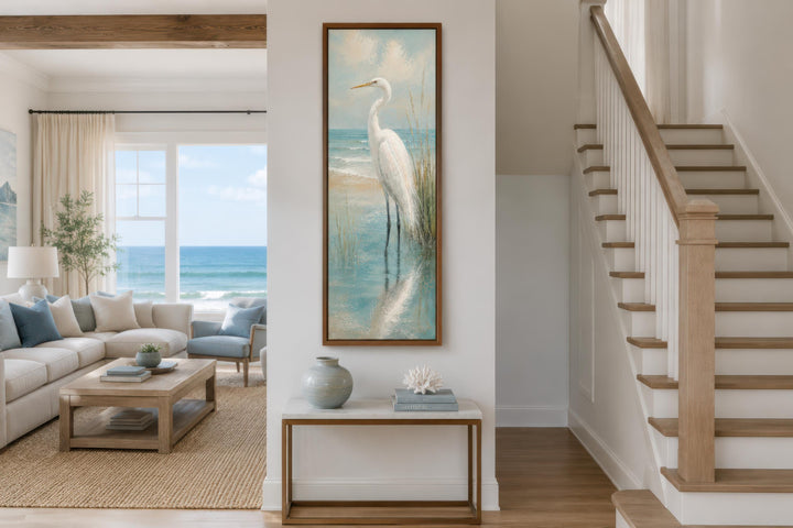 Tall narrow vertical canvas print of a white egret in teal coastal water on a white hallway wall.