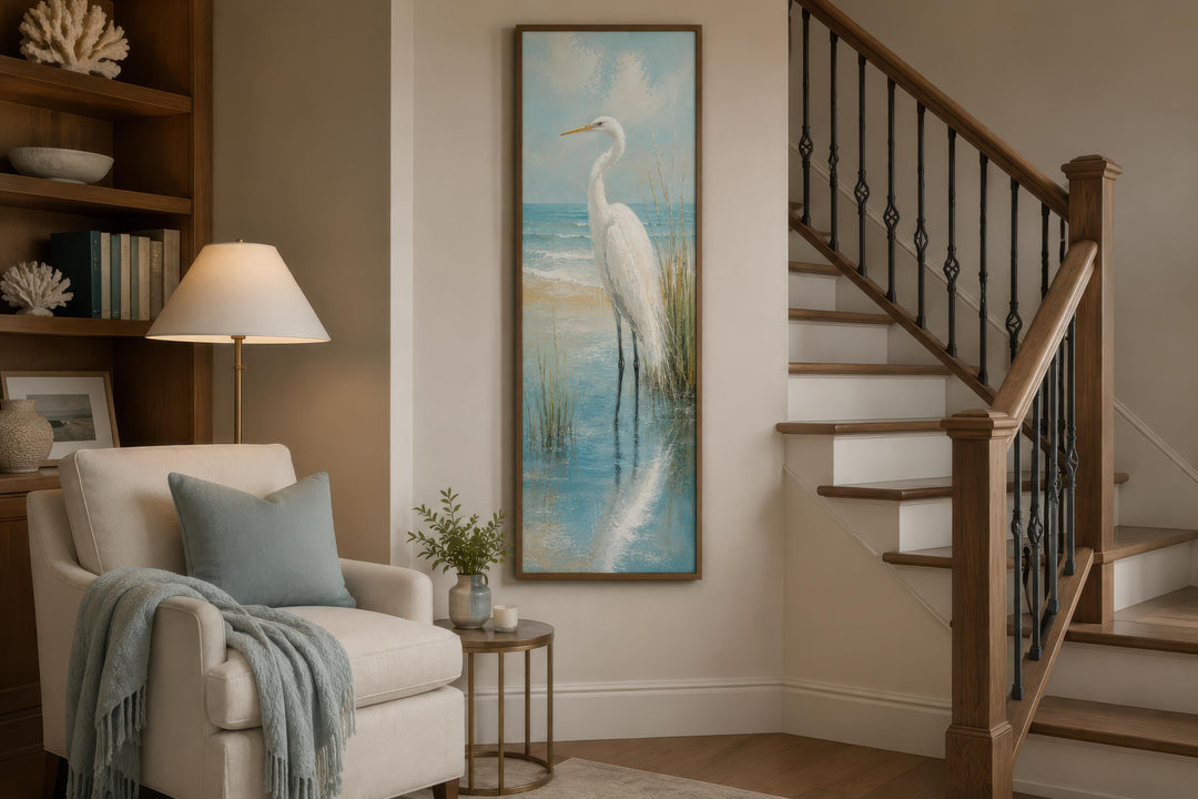 Tall narrow canvas print of a white egret in teal coastal water, hung in a beach house living room.
