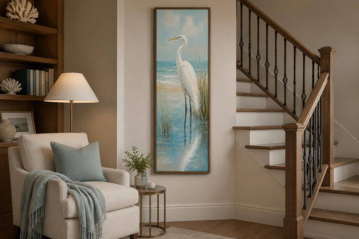 Tall narrow canvas print of a white egret in teal coastal water, hung in a beach house living room.