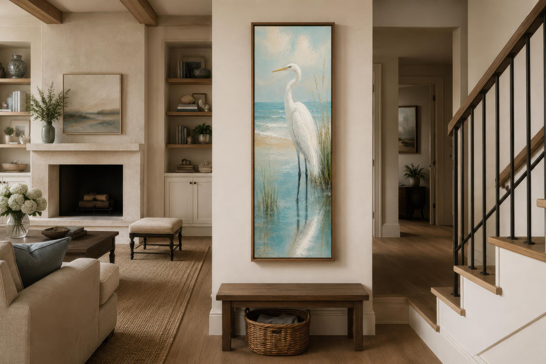 Tall narrow canvas print of a white egret in teal coastal water on a vertical wall in a living room.