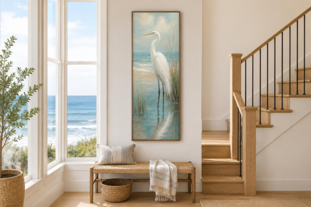 Tall narrow canvas print of a white egret in teal coastal water on a wall in a beach house entryway.