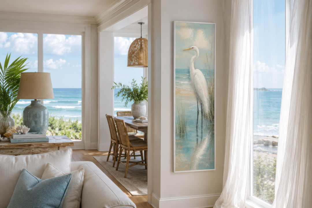 Tall narrow canvas print of a white egret standing in teal coastal water on a white wall.