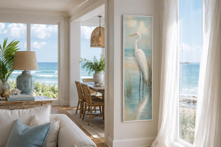 Tall narrow canvas print of a white egret standing in teal coastal water on a white wall.