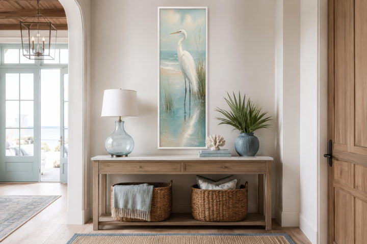 Tall narrow canvas print of a white egret in teal water, hung above a wooden console table.