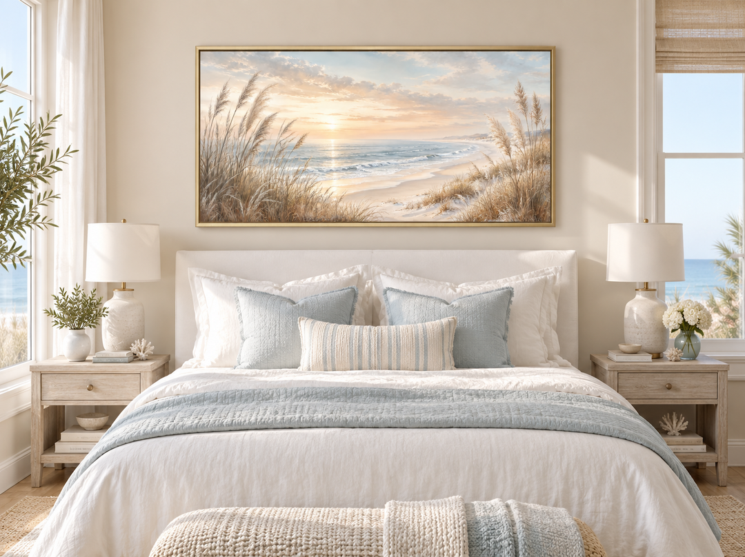 Framed beach pampas grass art above a bed with neutral coastal decor and soft blue accents.