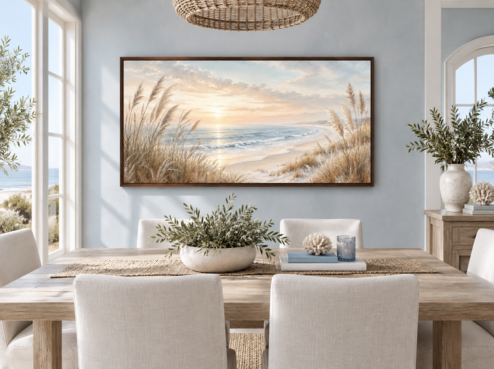 Framed coastal canvas print of a beach sunset with pampas grass above a wooden dining table.