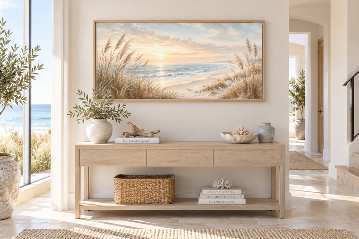 Framed coastal canvas print of beach pampas grass at sunset above a wooden console table.
