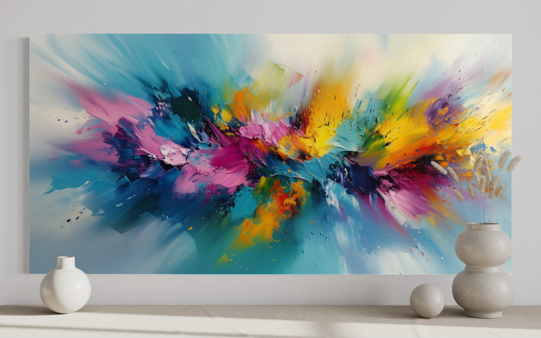 Vibrant abstract wall art with multicolored brushstrokes in blue, pink, and yellow on a white wall.