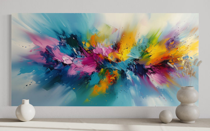 Vibrant abstract wall art with multicolored brushstrokes in blue, pink, and yellow on a white wall.