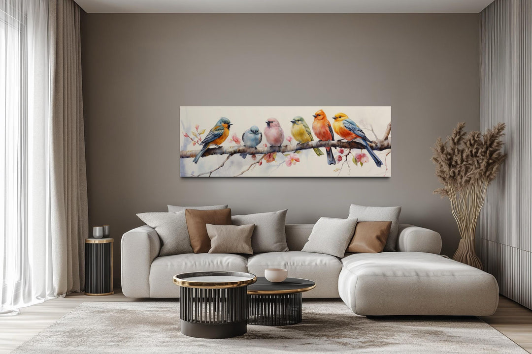 Colorful birds on a branch long horizontal wall art above a modern sofa in a neutral living room.