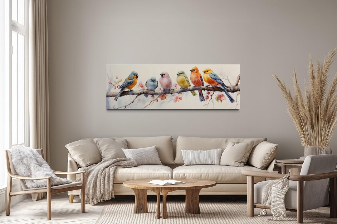 Colorful birds on a branch long horizontal wall art hanging above a beige sofa in a modern room.