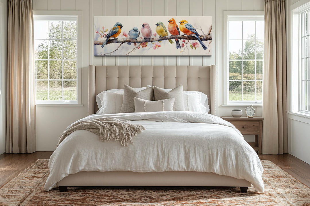 Colorful birds on a branch long horizontal canvas art hanging above a bed in a bright bedroom.