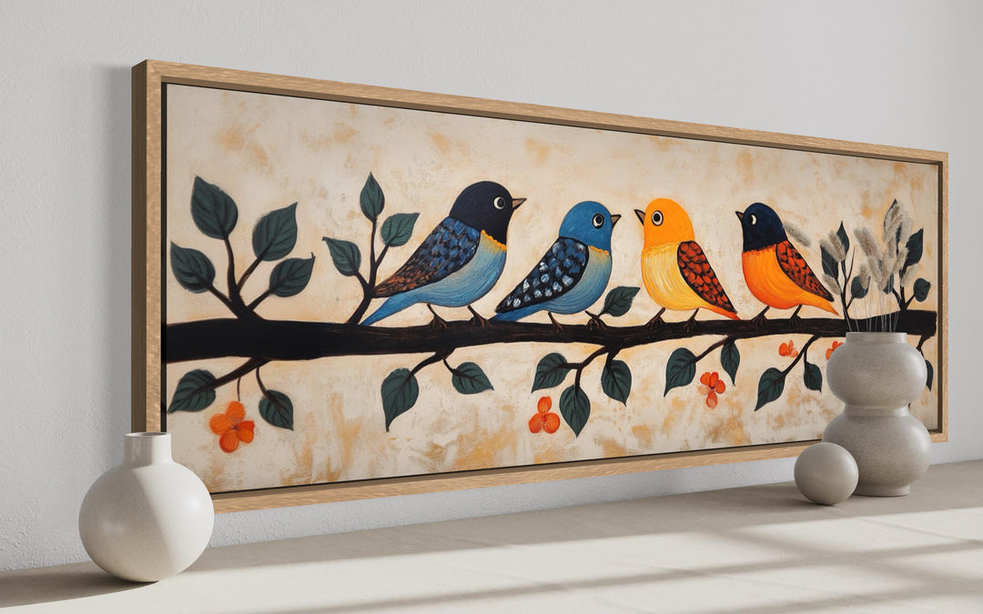Long narrow folk art canvas print of four colorful birds on a branch, framed in light wood.