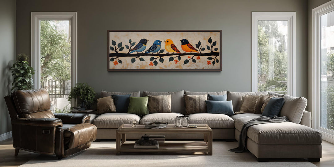 A long narrow canvas print of colorful folk-style birds perched on a branch above a sofa.