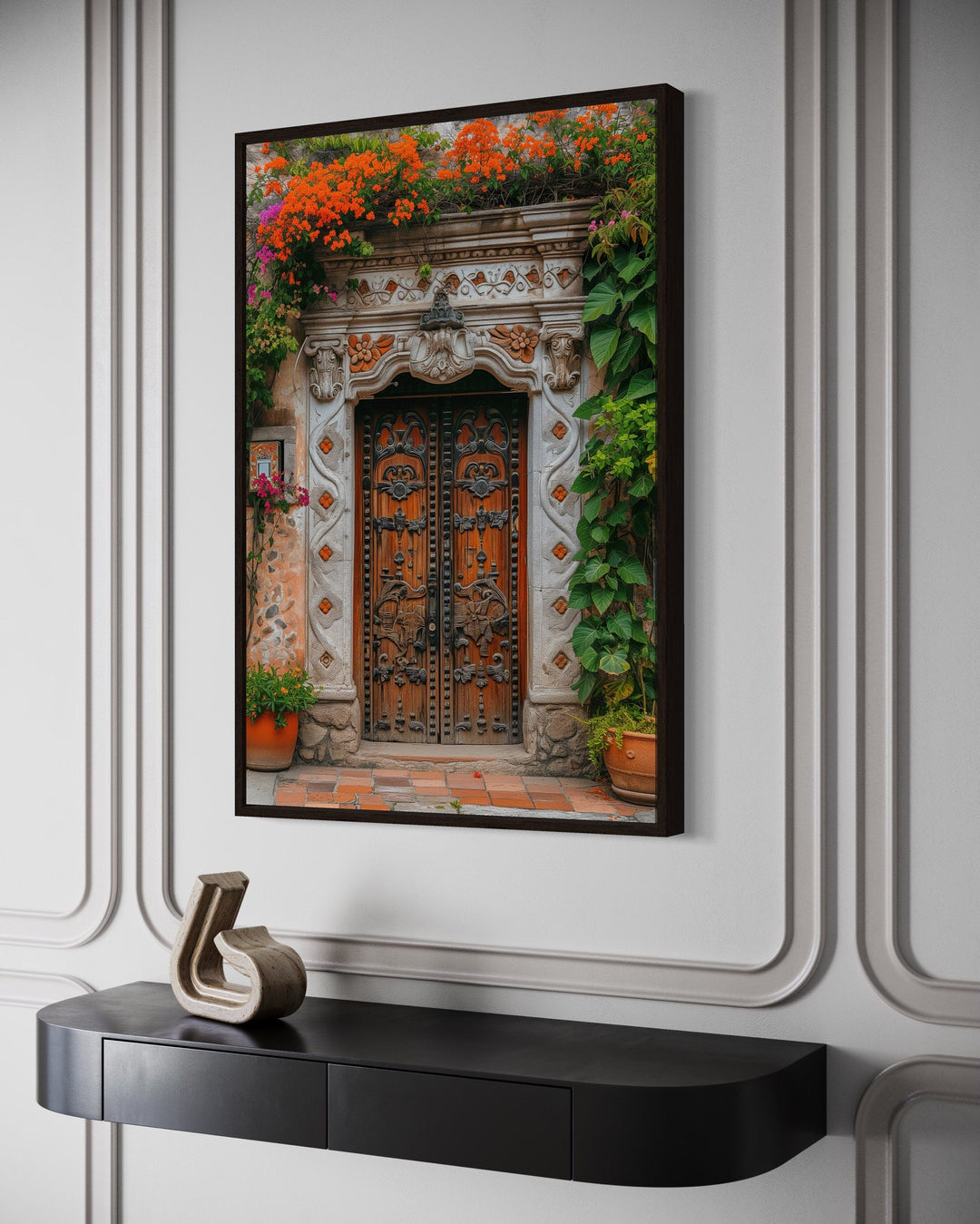Framed canvas wall art of a carved Mexican door with orange flowers above a black console table.