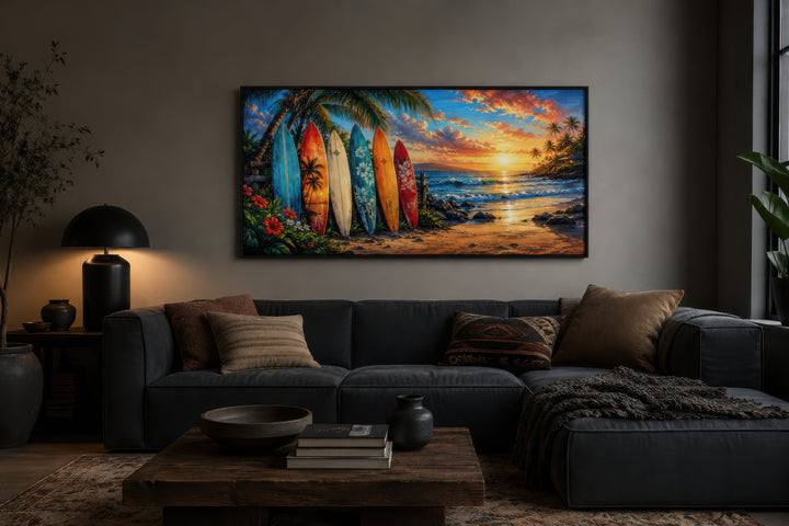 Colorful surfboards on a tropical beach at sunset framed canvas wall art above a dark grey sofa.
