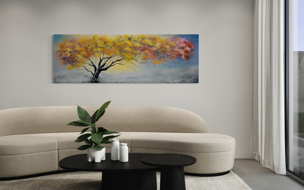 Colorful horizontal canvas wall art of a tree with yellow, pink, and orange leaves over a sofa.