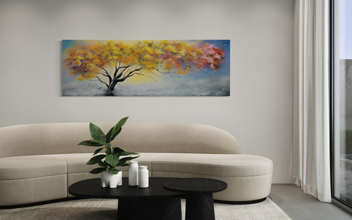 Colorful horizontal canvas wall art of a tree with yellow, pink, and orange leaves over a sofa.