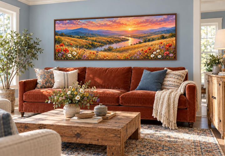 Panoramic canvas art of a wildflower meadow and river sunset above a rust-colored velvet sofa.
