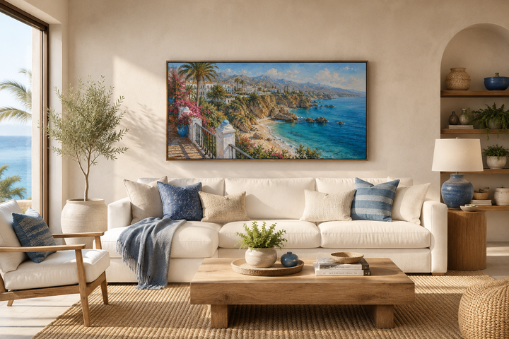 Framed canvas wall art of a Mediterranean coastal village above a white sofa in a coastal room.