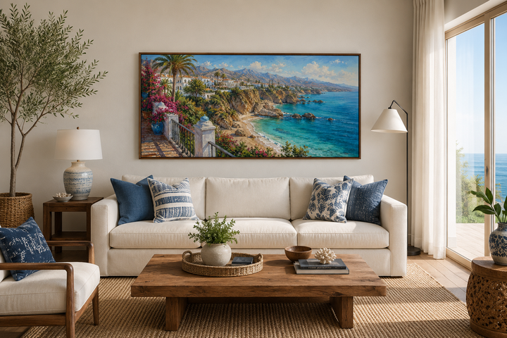 Framed canvas wall art of a Mediterranean coastal village above a white sofa in a coastal room.