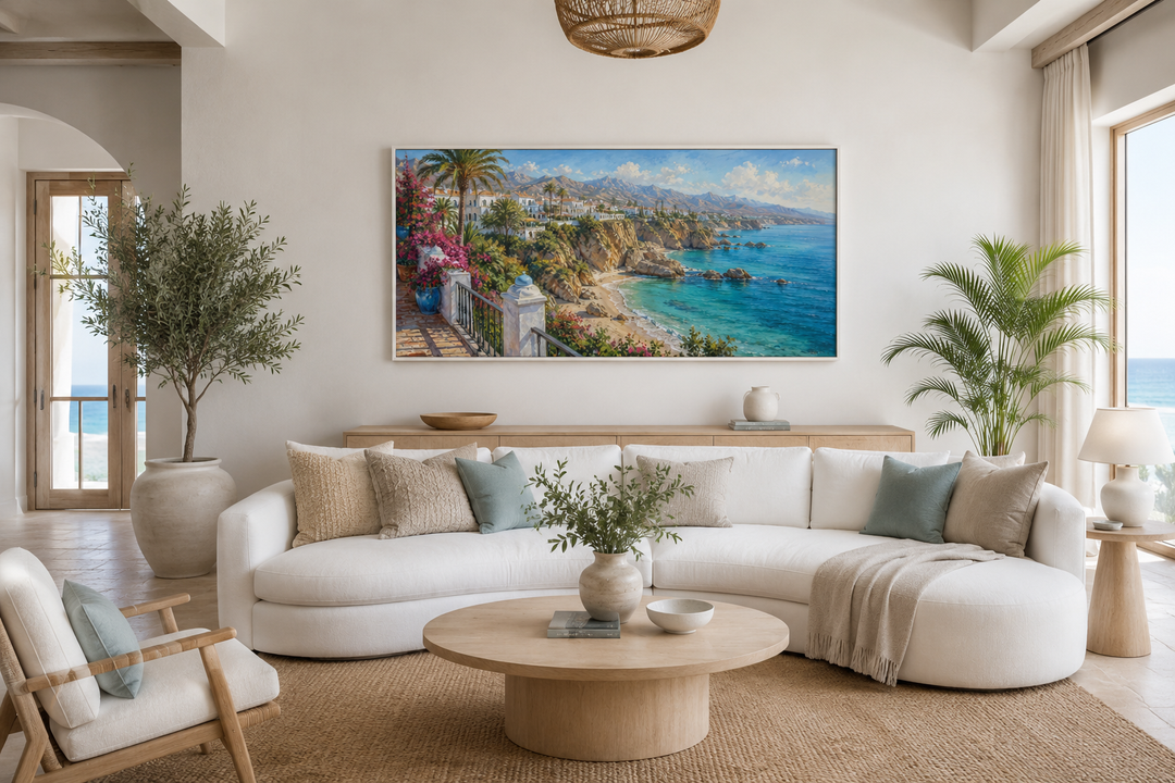 Framed canvas wall art of a sun-drenched Mediterranean coastal village above a white curved sofa.