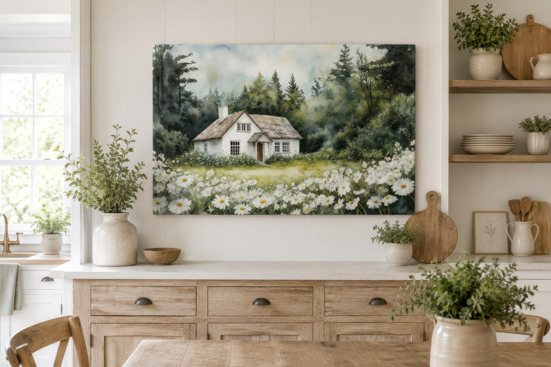 A watercolor canvas print of a white cottage in a daisy field hangs in a rustic farmhouse kitchen.