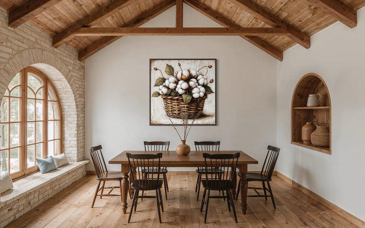 Square canvas wall art of cotton bolls in a wicker basket centered in a rustic farmhouse dining room.