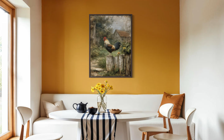A framed canvas print of a rooster on a fence hangs on a yellow wall above a modern dining nook.