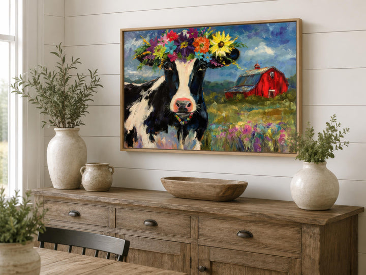 Whimsical oil painting of a cow with a flower crown on a canvas above a rustic wooden sideboard.