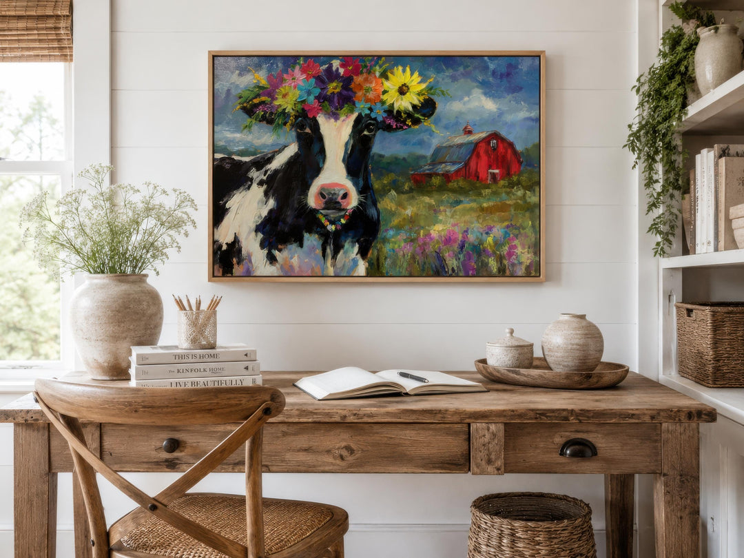 Whimsical cow canvas art with a flower crown hangs above a rustic wooden desk in a farmhouse office.