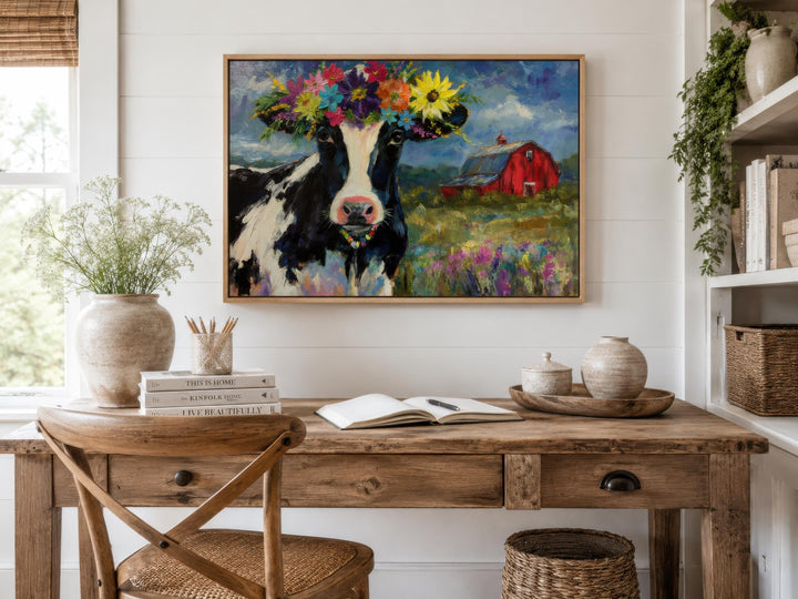 Whimsical cow canvas art with a flower crown hangs above a rustic wooden desk in a farmhouse office.
