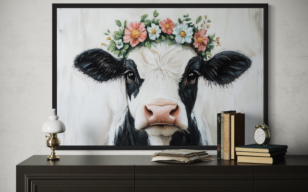 Cow with floral wreath canvas wall art in a black frame above a dark wood console table.
