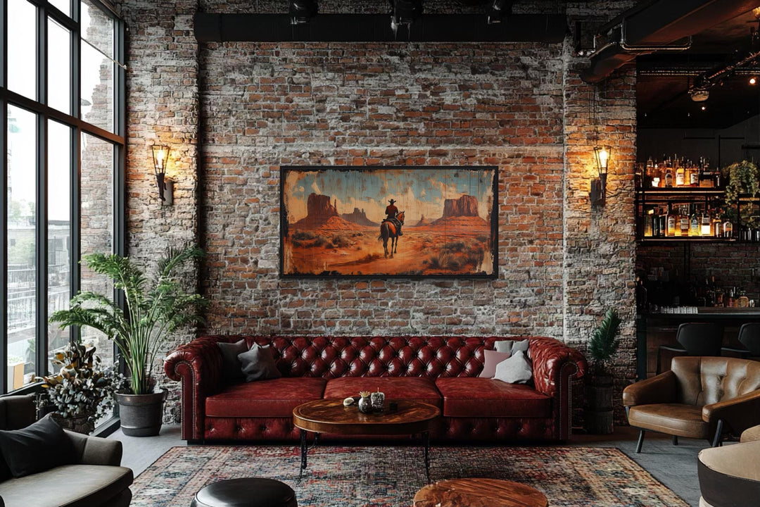 Cowboy riding a horse in Monument Valley framed canvas wall art on a brick wall above a red sofa.