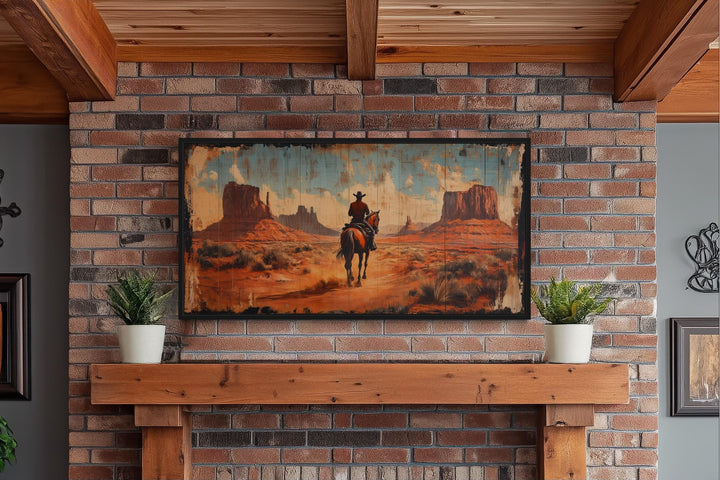 Framed panoramic canvas art of a cowboy on a horse in Monument Valley above a brick fireplace.