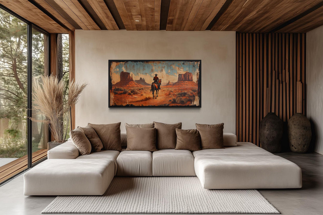 Framed canvas wall art of a cowboy riding a horse in Monument Valley above a modern sectional sofa.