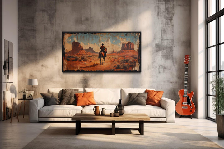 Panoramic framed canvas art of a cowboy on horseback in Monument Valley above a white sofa.