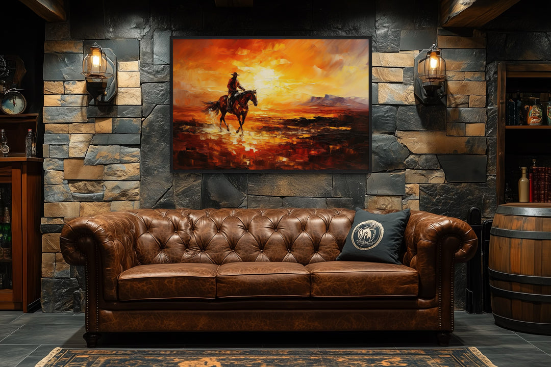 Wild West canvas art of a cowboy riding a horse at sunset, hung above a brown leather sofa.