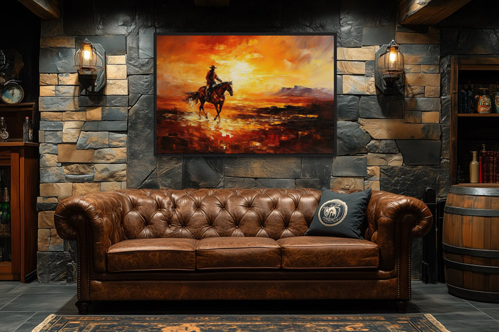 Wild West canvas art of a cowboy riding a horse at sunset, hung above a brown leather sofa.