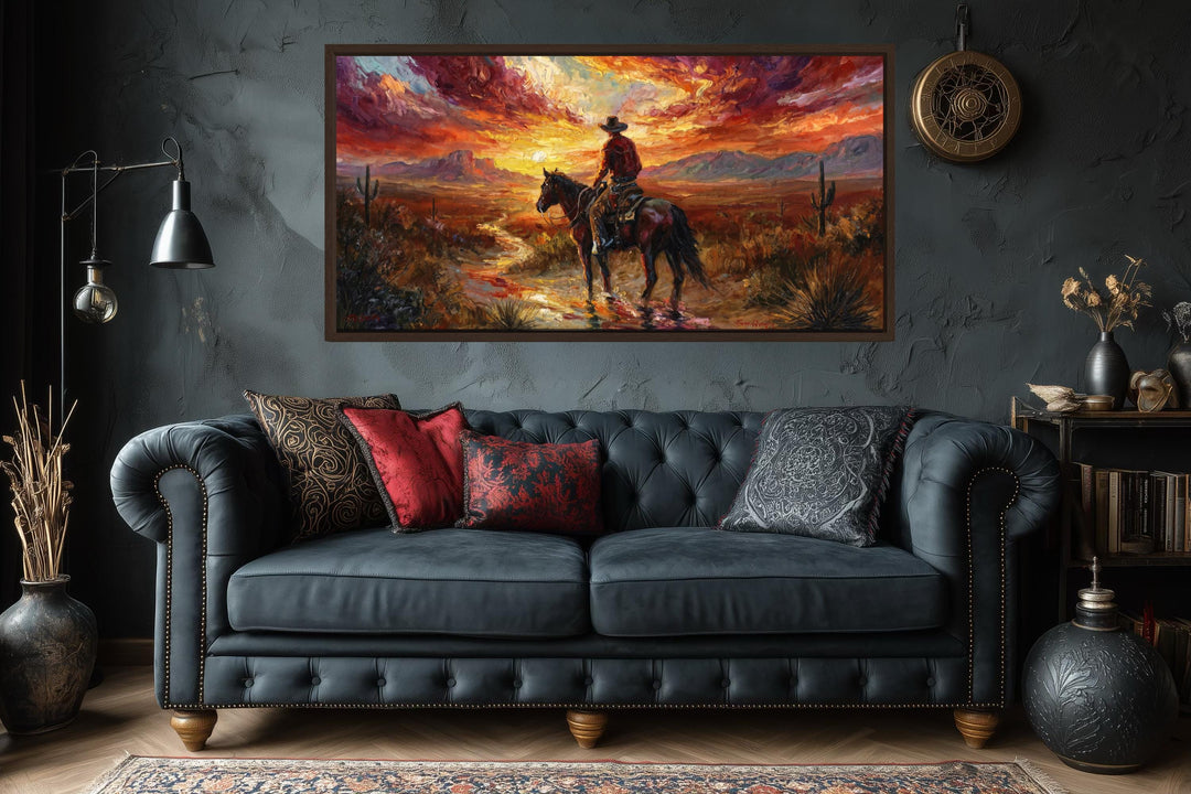 A framed canvas of a cowboy riding through a desert sunset hangs above a dark tufted leather sofa.