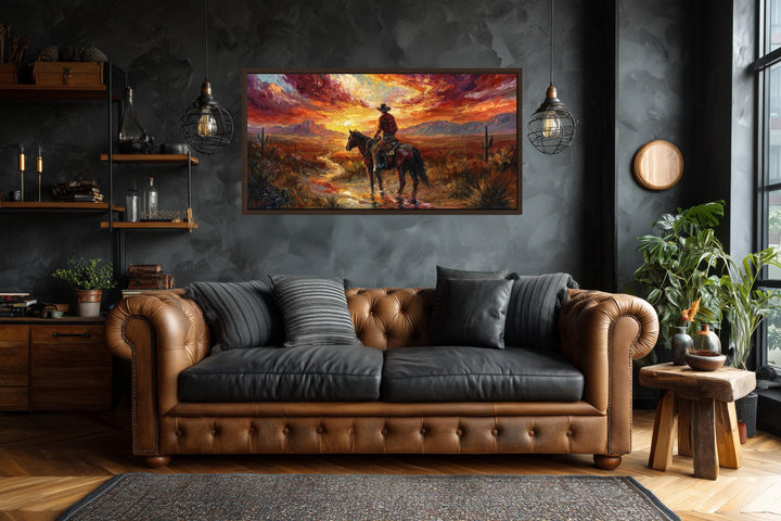 A framed canvas of a lone cowboy riding through a desert at sunset above a brown leather sofa.
