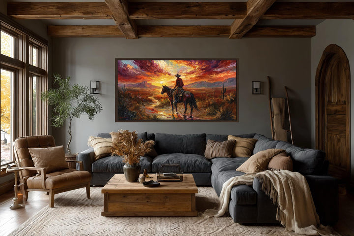 A wide horizontal canvas of a cowboy riding through a desert sunset hangs in a rustic living room.