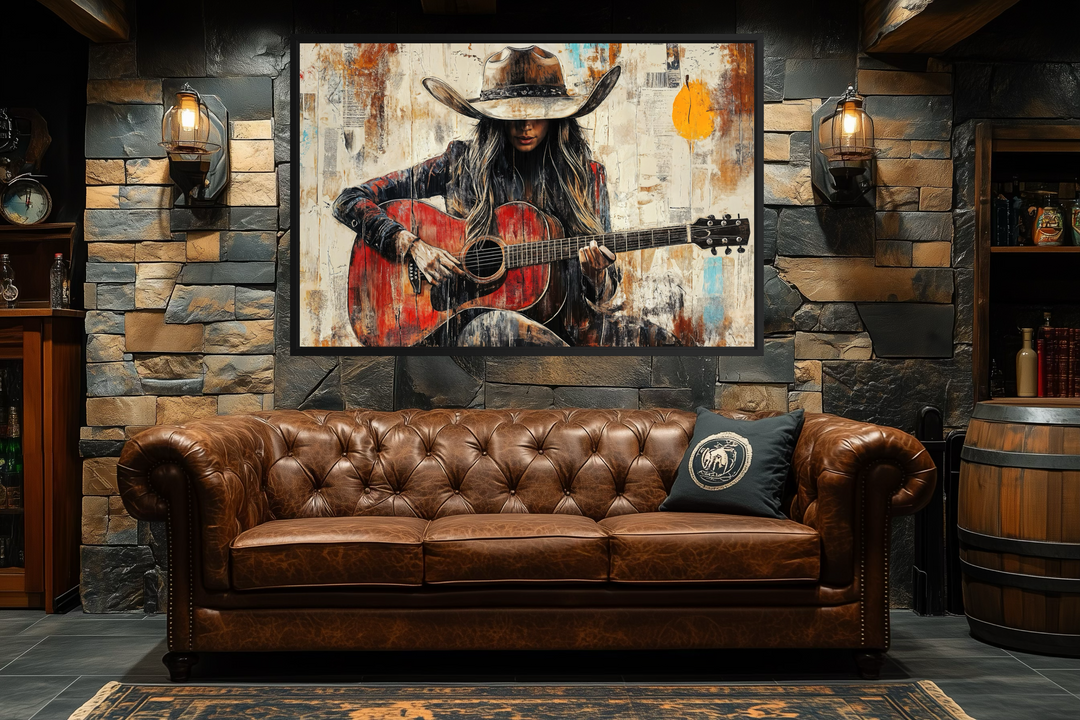 Framed canvas wall art of a cowgirl playing a red guitar above a brown leather chesterfield sofa.