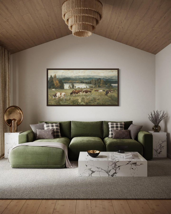 A large horizontal canvas painting of cows grazing in a lush pasture, framed in dark wood.