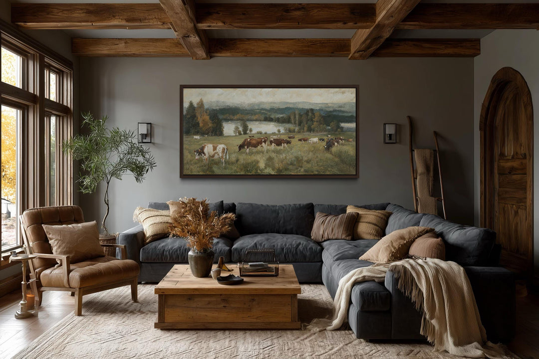 A large horizontal canvas painting of cows grazing in a pasture hangs in a rustic living room.