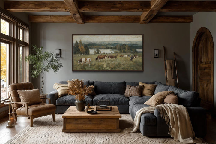 A large horizontal canvas painting of cows grazing in a pasture hangs in a rustic living room.
