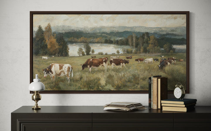 A large horizontal canvas painting of cows grazing in a lush pasture with a lake and hills.